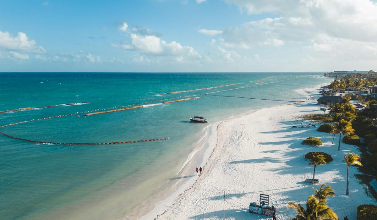 A beautiful aerial view of Playa del Carmen's white sandy beach with clear blue waters and palm trees swaying in the tropical breeze.